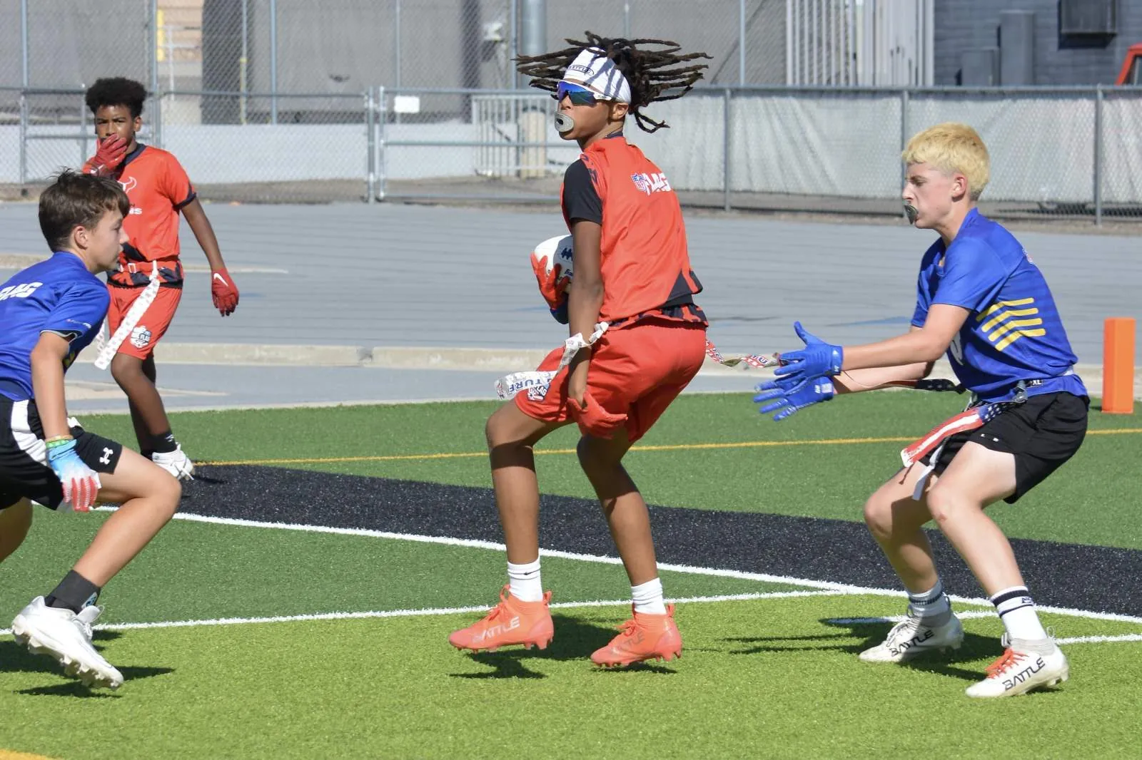 Receiver in an official NFL FLAG jersey hauling in a catch mid-air between two defenders